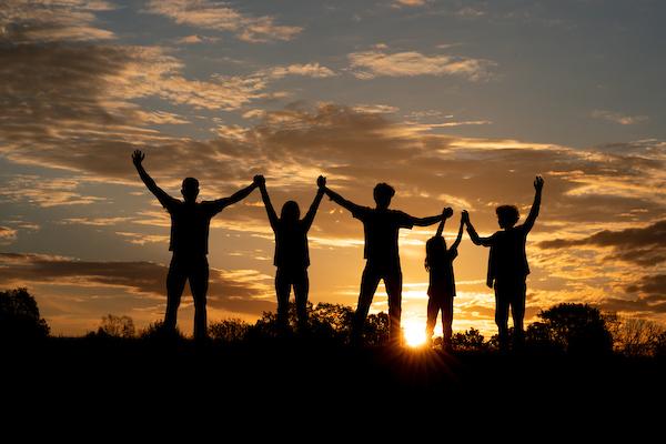 family backlit by sunset, with arms in the air