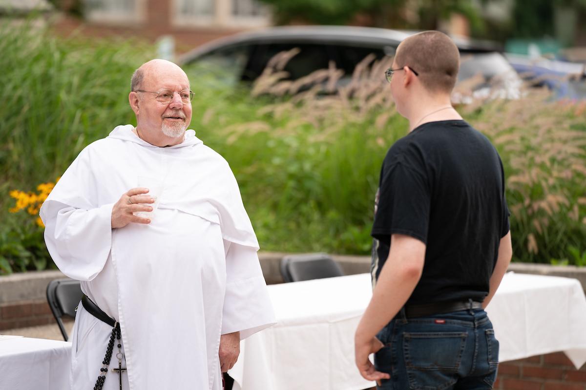 穿着白色长袍的斯坦神父在外面对一个学生说话
