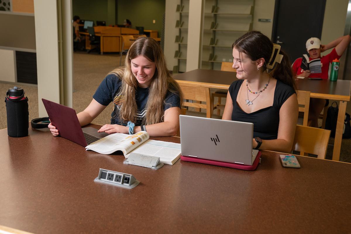 两个学生微笑着，拿着笔记本电脑和书聊天